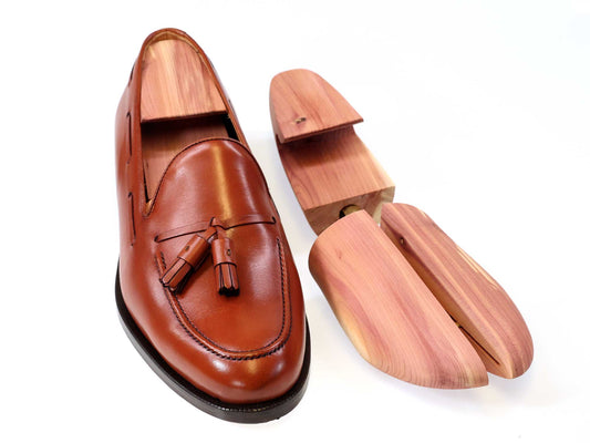 A brown leather loafer with tassels is displayed beside Cathcart Elliot Mens Cedar Wood Adjustable Width Split-toe Hook-Heel Shoe Trees UK, shown in two pieces on a white background to highlight their structure.