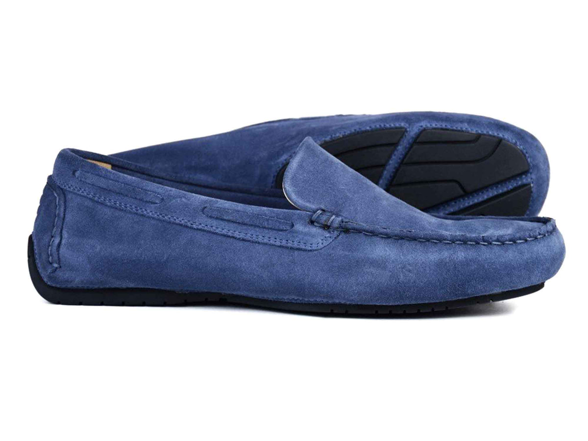 A pair of Orca Bay Silverstone Men’s Dark Denim Suede Driving Loafers by Orca Bay, with one loafer lying flat and the other positioned on its side to display the black rubber sole featuring a textured pattern.