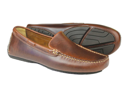 The Silverstone Men's Driving Loafer in Elk Pull-Up Leather by Orca Bay features visible stitching and a sturdy black rubber sole, shown with one shoe upright and the other displaying the sole on a white background. Perfect men’s brown driving shoes.