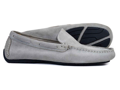 The Orca Bay Silverstone Men's Grey Suede Driving Loafer by Orca Bay is shown with one shoe lying flat and the other on its side to display the black rubber sole.