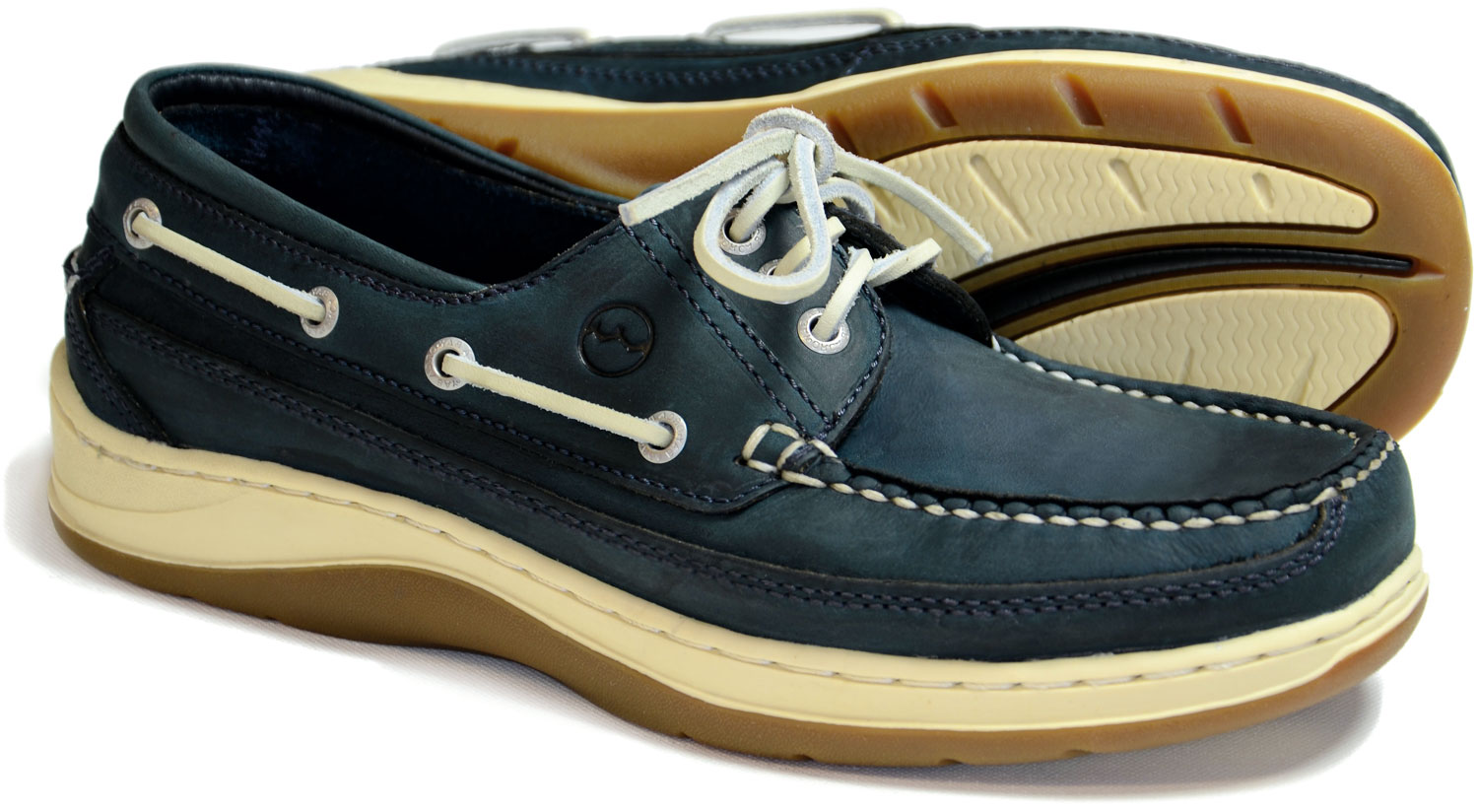 The SQUAMISH by Orca Bay are navy blue mens performance boat shoes featuring white laces, stitching, tan non-marking rubber soles, eyelet detailing on the sides, and a cushioned footbed. One shoe stands upright while the other is tilted on its side.