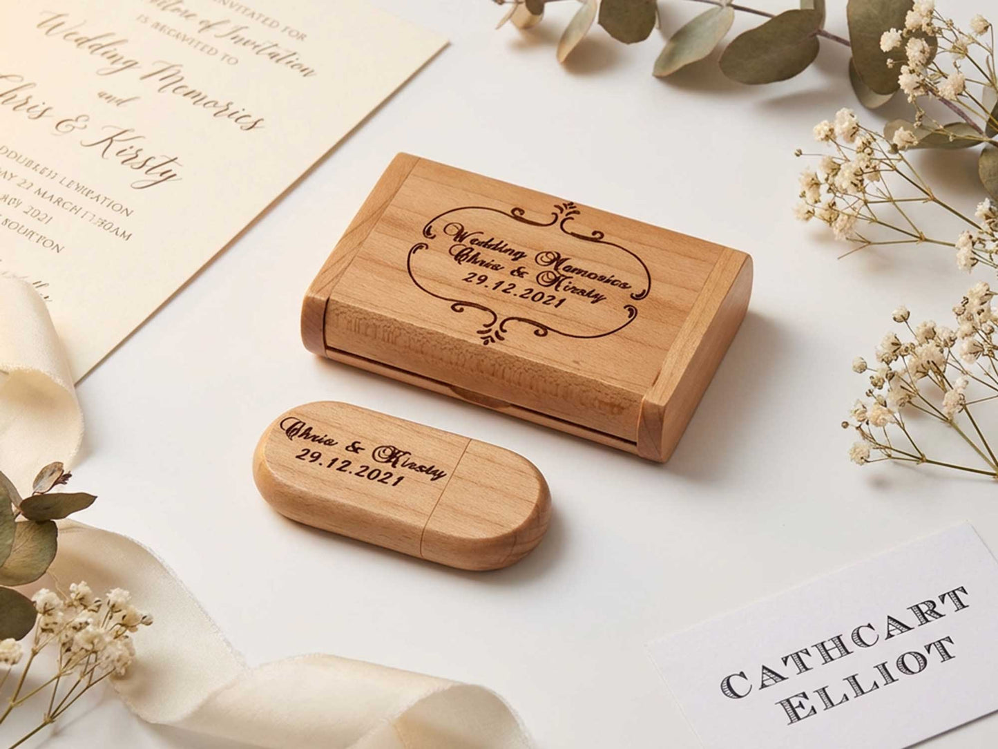 The Cathcart Elliot Personalised Maple Wood 16GB USB 3.0 with matching engraved gift box is shown on a light surface, surrounded by invitations, ribbon, and dried flowers. Engraving reads: “Wedding Memories Chris & Kirsty 29.12.2021.”.