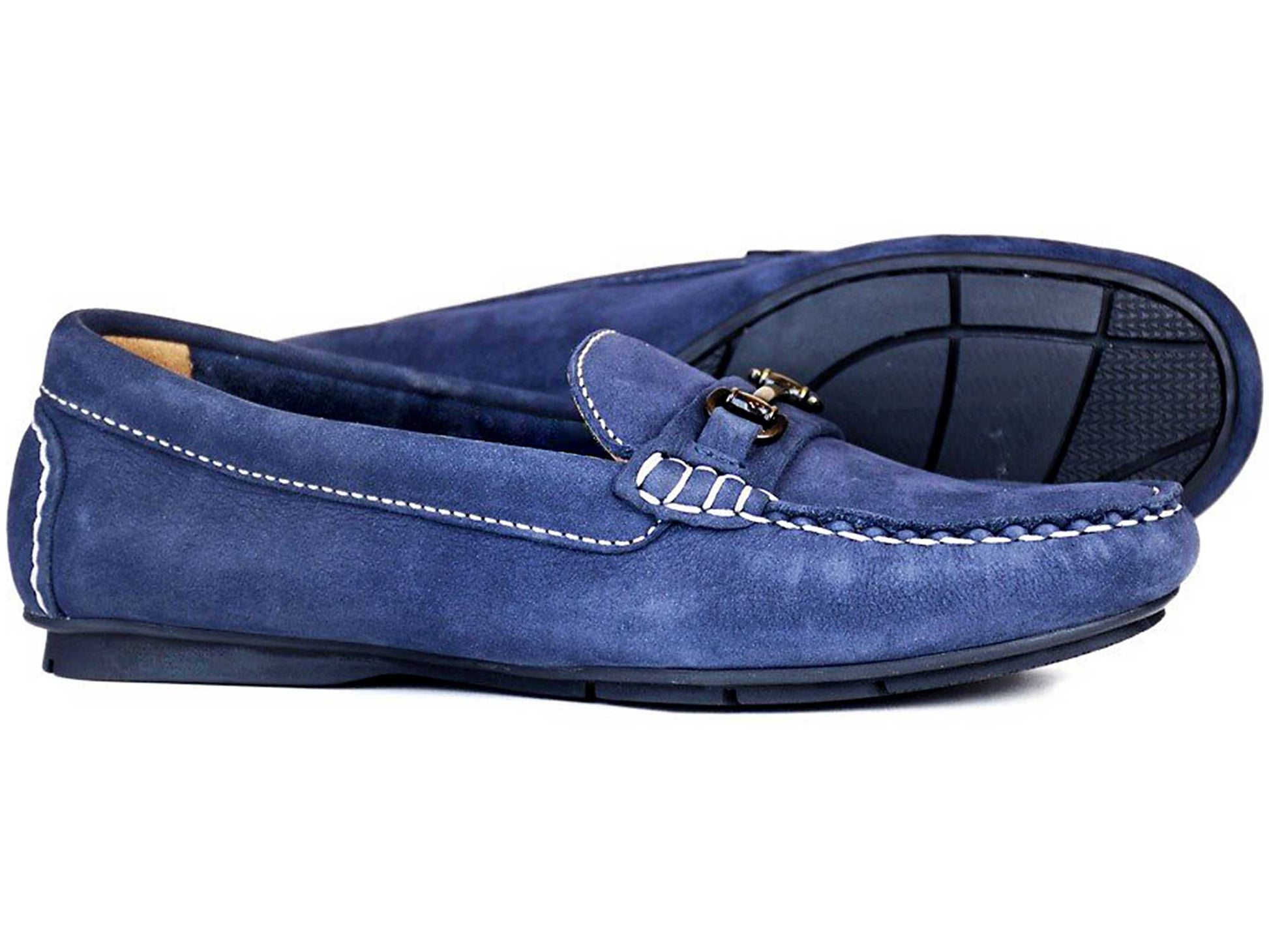 A pair of Orca Bay VERONA Ladies Loafers in Indigo Nubuck with white stitching, black rubber soles, and a metal bit detail. One shoe is flat while the other stands upright, highlighting the unique sole pattern and sleek, casual design.