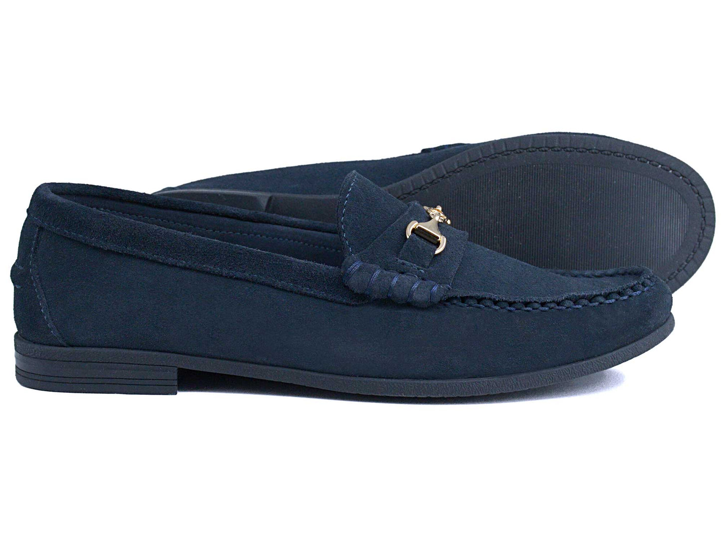 The Orca Bay Zurich Ladies Navy Suede Buckle Loafer features black soles, a decorative metal bit, and visible front stitching. One lightweight Orca Bay loafer stands upright while the other rests on its side.